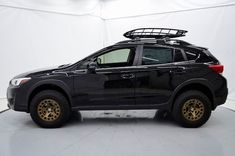 a black suv with gold rims is parked in a white room and it has a basket on the roof