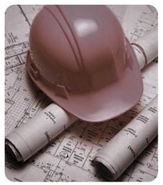 a hard hat sitting on top of blueprints next to rolled up construction plans