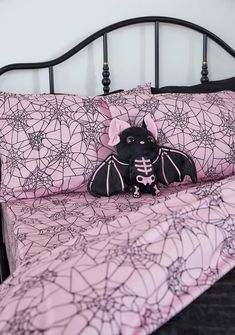 a black cat stuffed animal sitting on top of a pink bedspread in a bedroom