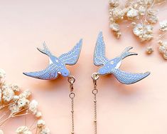 two blue birds with chains hanging from them on a pink surface next to white flowers