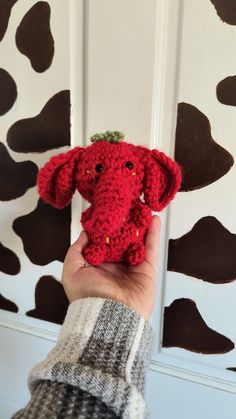 a hand holding a red stuffed animal in front of a cow print wallpapered door