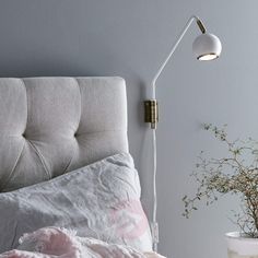 a bed with a pink blanket and a white lamp on the wall next to it