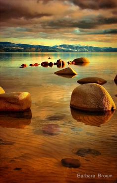 some rocks are in the water and there is a cloudy sky above them with mountains in the distance