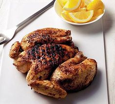 grilled chicken on a white plate next to a bowl of oranges and silverware