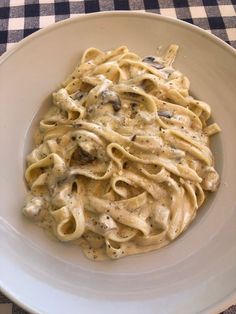 a white plate topped with pasta covered in sauce and mushrooms on top of a checkered table cloth