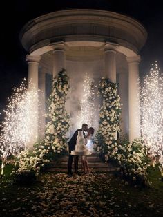 a bride and groom kissing in front of a gazebo with white flowers on it