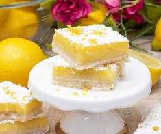 three pieces of lemon bars sitting on top of a white plate next to some flowers