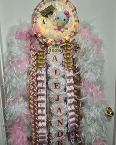 a hello kitty themed door hanger with pink, white and gold feathers on it