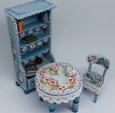 a doll house furniture set including a table and chair with flowers on the top, an open bookcase behind it