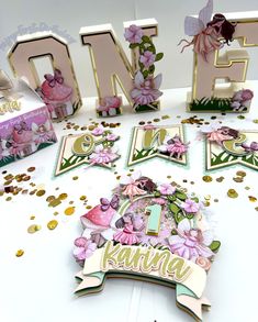 some pink and gold decorations on top of a white table with confetti around it