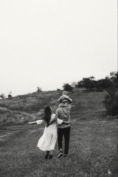 a man and woman walking through a field holding hands