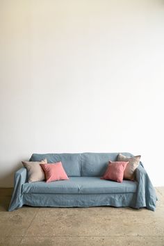 a blue couch with three pillows on it in front of a white wall and concrete floor