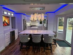 a large kitchen with white cabinets and blue lights on the ceiling, along with a dining room table surrounded by bar stools