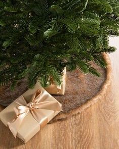 a christmas tree with presents under it on a wooden floor next to a potted plant