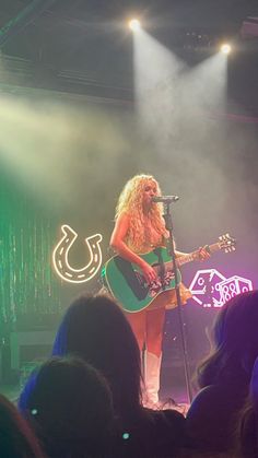 a woman on stage with a guitar and microphone