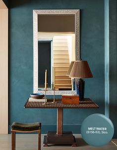 a table with a lamp and mirror on it in front of a blue painted wall