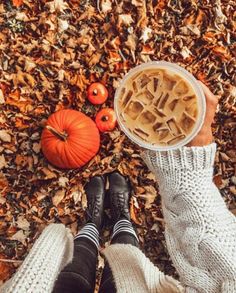 a person standing in leaves with their feet on the ground holding a cup of coffee