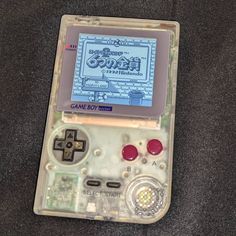 an old nintendo gameboy sitting on top of a gray cloth covered floor next to a remote control