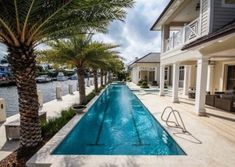 an empty swimming pool in front of a large house with palm trees and chairs around it