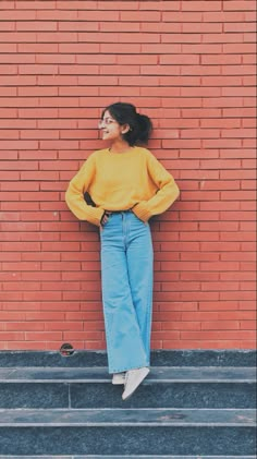 a woman leaning against a brick wall with her hands on her hips and looking up