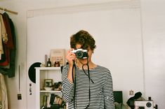 a woman taking a photo in front of a mirror with a camera on her shoulder