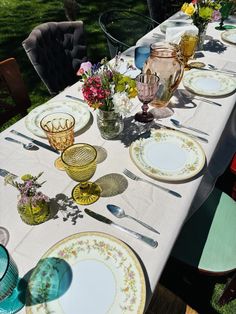 the table is set with plates, cups and vases on it for an outdoor meal