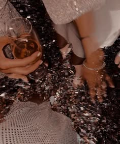 two hands holding a glass of wine on top of a table covered in confetti