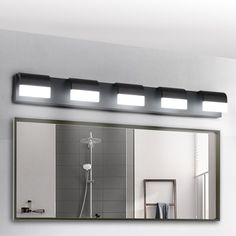 a bathroom mirror with three lights above it and a shower head in the reflection on the wall