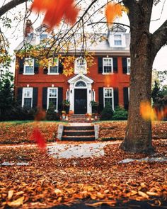 a large red brick house surrounded by trees and leaves on the ground in front of it