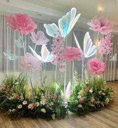 some pink and white flowers are in the middle of a wooden floor with curtains behind them