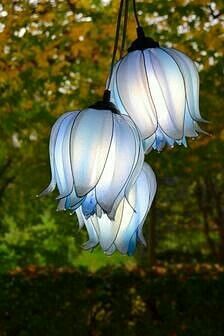 three lights hanging from the ceiling in front of trees with leaves on them and one light blue