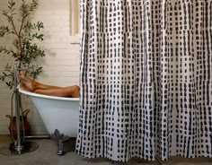 a person laying down in a bathtub next to a shower curtain with black and white squares on it