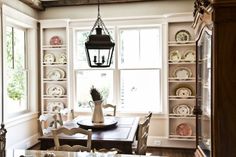 the dining room table is surrounded by white china and glass shelves that are filled with dishes