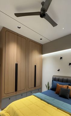 a bed sitting under a ceiling fan in a bedroom next to wooden cabinets and drawers