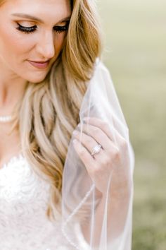 a beautiful blonde woman wearing a veil and holding her wedding ring on her finger while standing in the grass