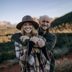 a man and woman standing next to each other in front of a mountain with trees