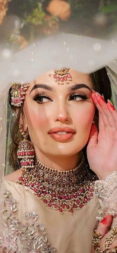 a woman in a bridal gown with jewelry on her head and hands near her face