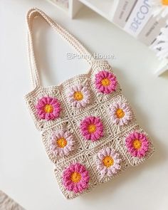 a crocheted purse with pink and yellow flowers on the front, sitting on a table