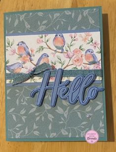 a hello card with blue birds and flowers on it, sitting on top of a wooden table