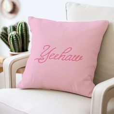 a pink pillow sitting on top of a white chair next to a potted cactus