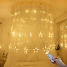 a person holding a remote control in front of a bed with lights on the ceiling