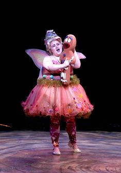 a woman dressed as a fairy holding a teddy bear in her arms and wearing a pink dress