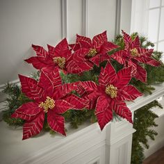 red poinsettia and greenery sit on a mantle in front of a window