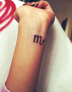 a woman's wrist tattoo with the letter m on it