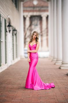 a woman in a long pink dress standing on a brick walkway with her arms crossed