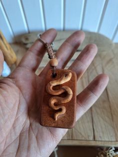 a hand holding a wooden pendant with the word snake on it