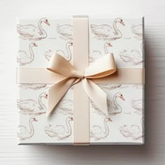 a gift wrapped in white paper with a pink ribbon and a swan design on it