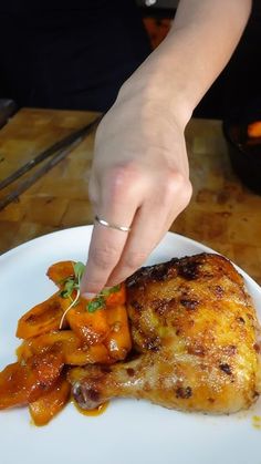 a person is picking up some food on a white plate with carrots and potatoes