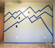 an empty room with blue tape on the wall and mountains painted on the wall behind it