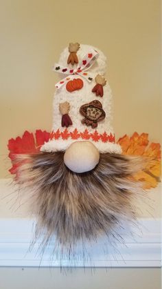 a stuffed animal wearing a knitted hat on top of a mantle with autumn leaves around it